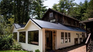 A rustic cabin with a sloped metal roof, large windows, and a brick pathway leading to the entrance. - Outpost Inn (Highlands)