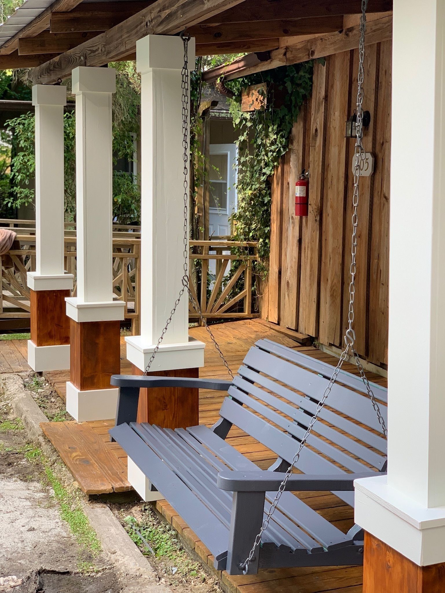 A wooden deck with a bench and white pillars.