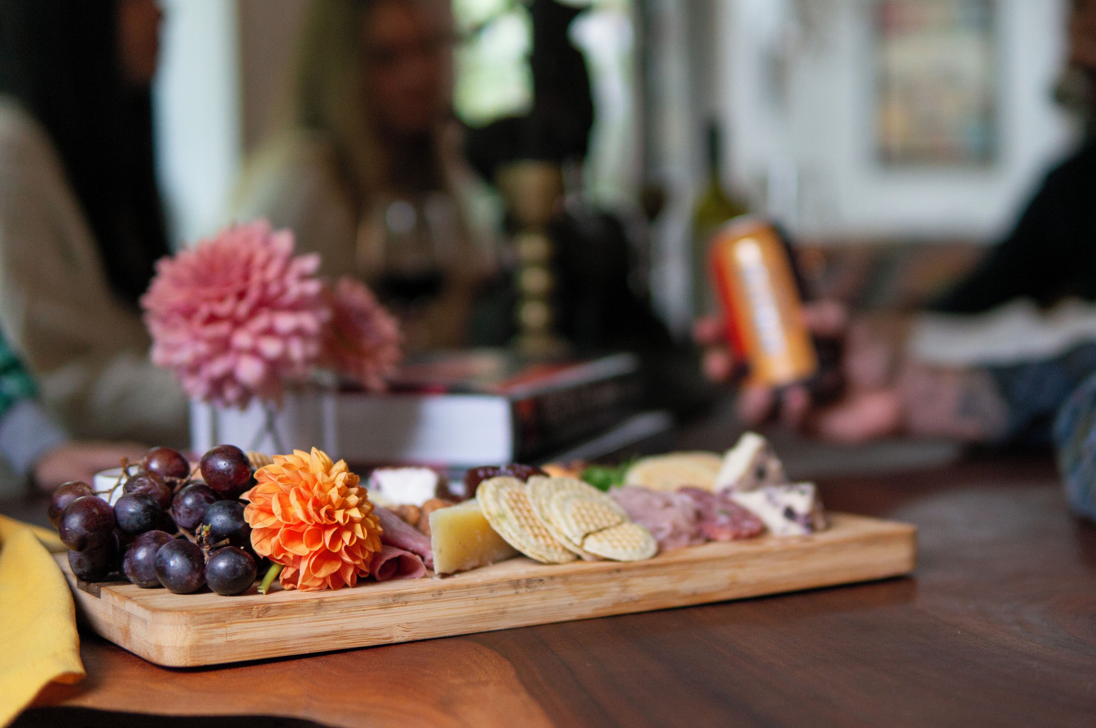 A wooden board with various cheeses, crackers, and grapes.