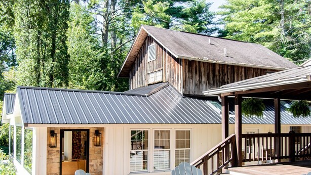 A rustic cabin with a metal roof, a deck with Adirondack chairs, and a fire pit. - Outpost Inn (Highlands)