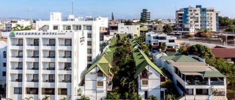 A multi-story hotel with a distinctive green roof and white facade, located in an urban area with other buildings in the background.