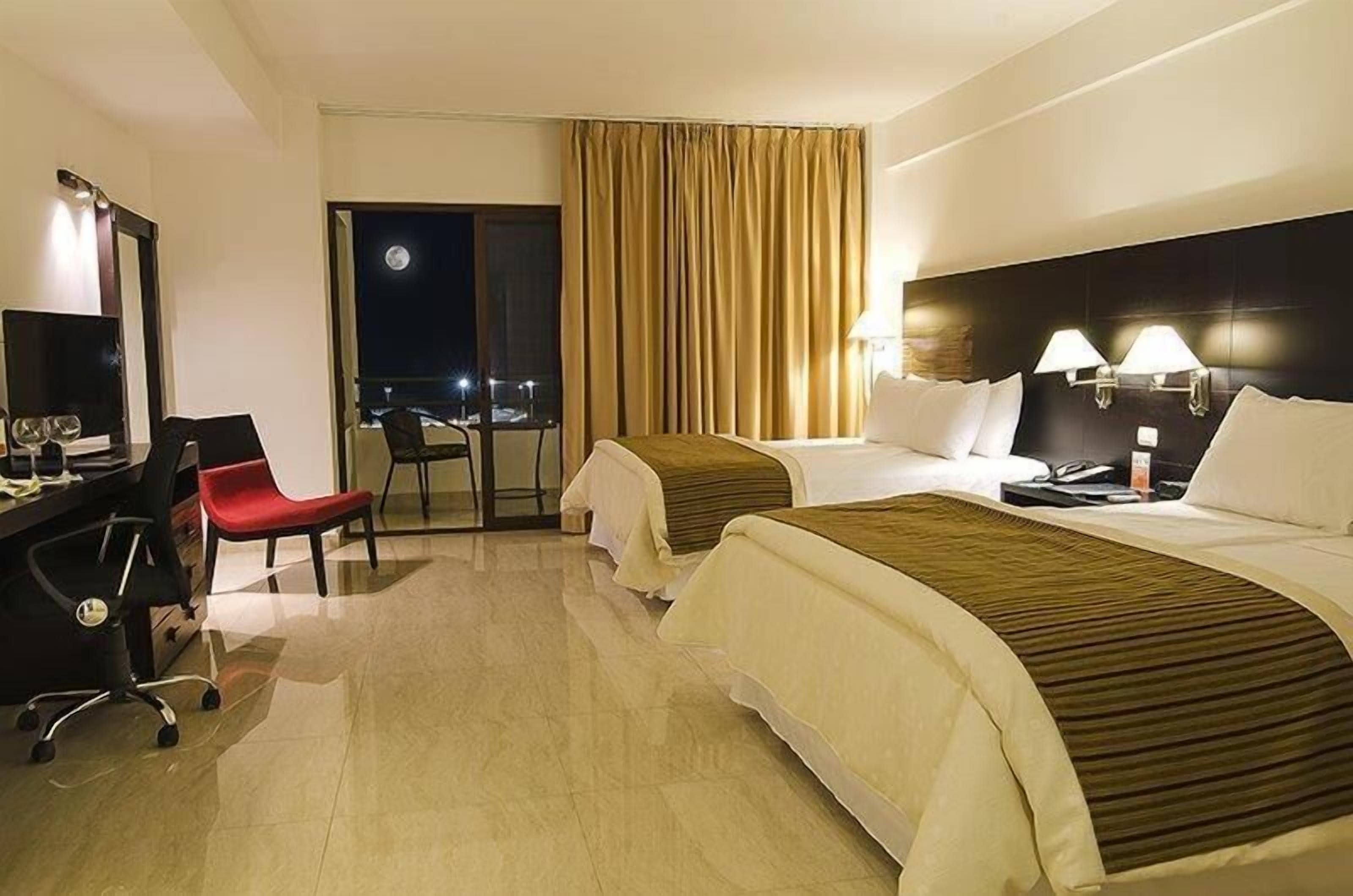 Une chambre d’hôtel avec deux lits, un bureau avec une chaise, une lampe de bureau et une table de chevet.