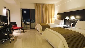 A hotel room with two beds, a desk with a chair, a desk lamp, and a nightstand.
