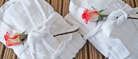 Zwei weiße Bademäntel, jeder mit einer Rose.