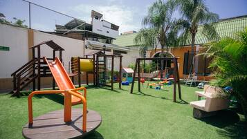 Children can play safely in this enclosed area with a slide, swings, and a seesaw on artificial turf.