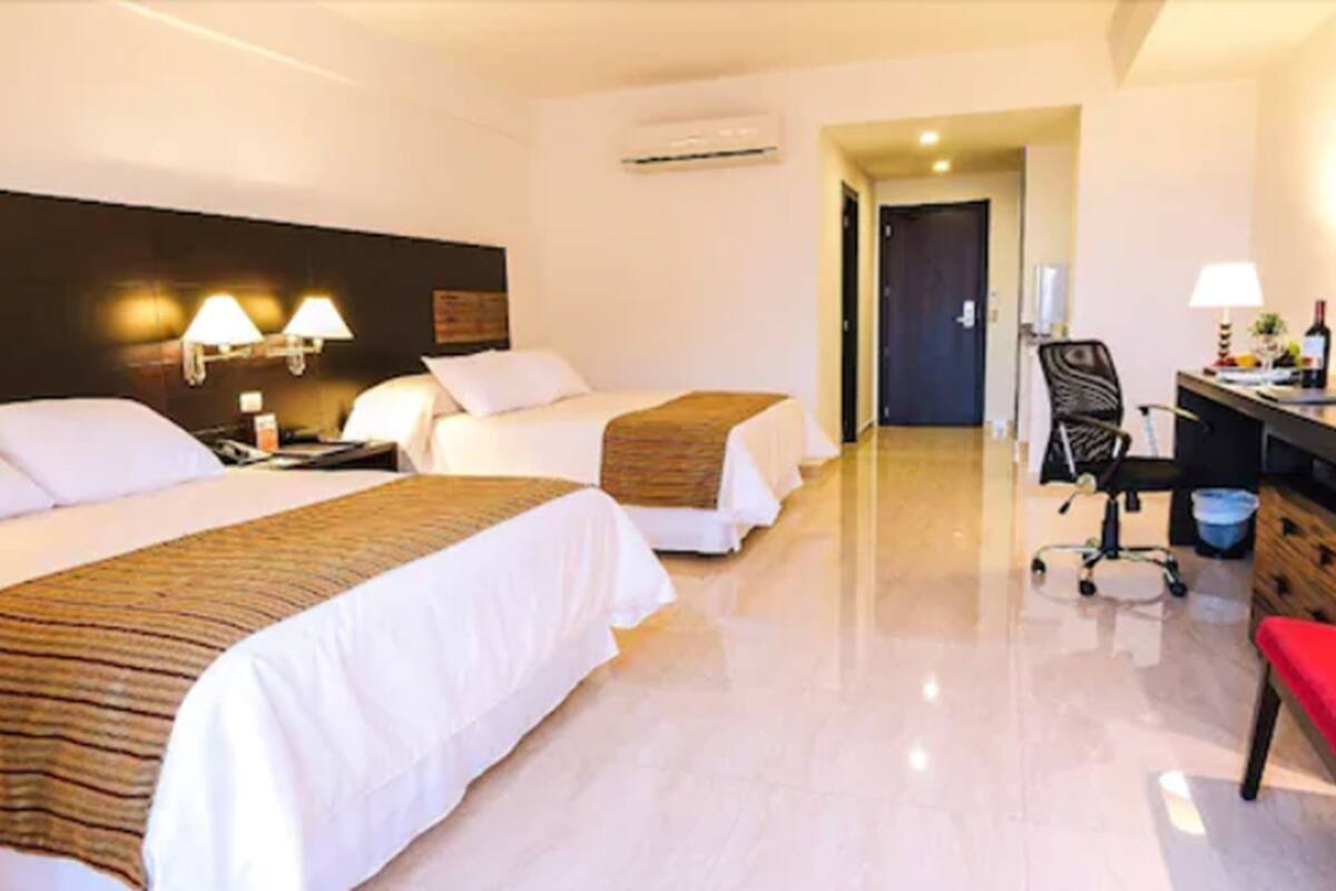 A hotel room with two beds, a desk with a chair, and an air conditioning unit.
