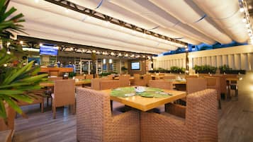 Een ruim restaurant met hoge plafonds, meerdere eettafels en comfortabele rieten stoelen.