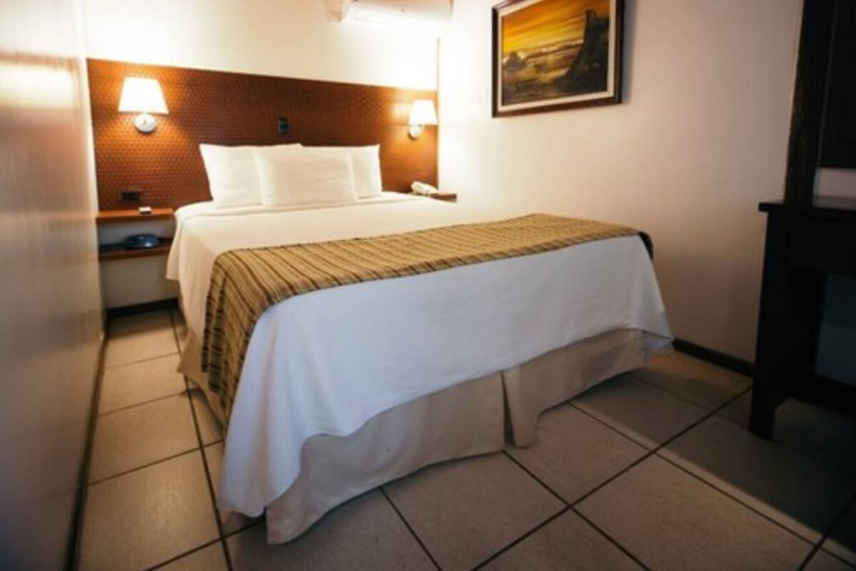A hotel room with a bed, two bedside lamps, a nightstand, and a painting on the wall.
