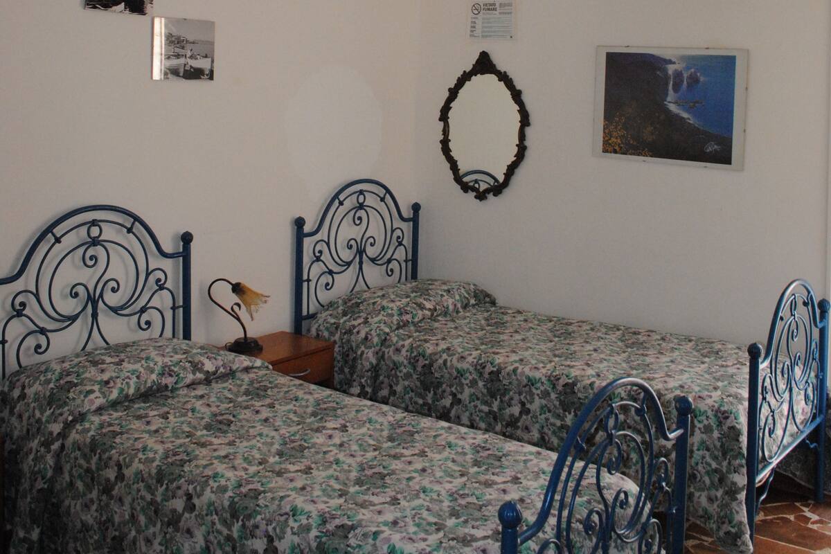 Un dormitorio con dos camas, una araña, aire acondicionado instalado en la pared y cuadros enmarcados.