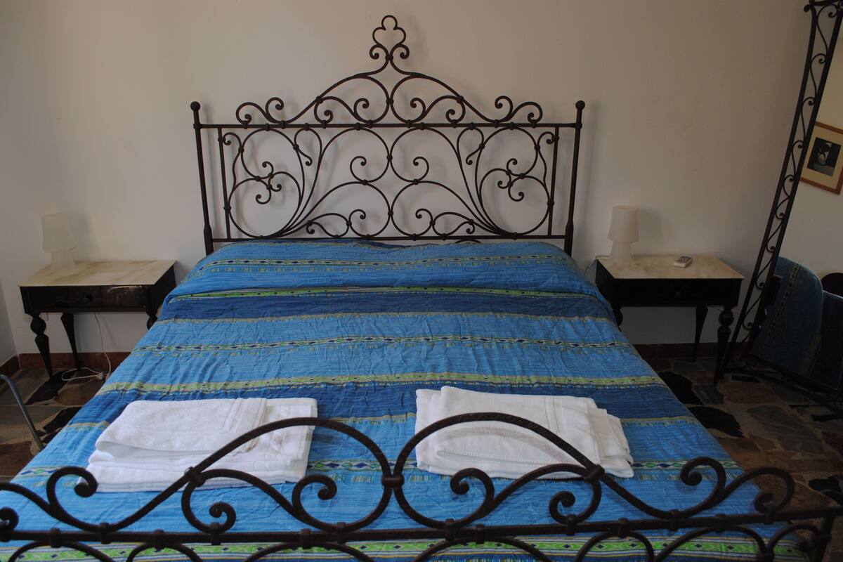 Una cama con un edredón azul y verde a rayas, dos toallas blancas y un cabecero decorativo de metal.