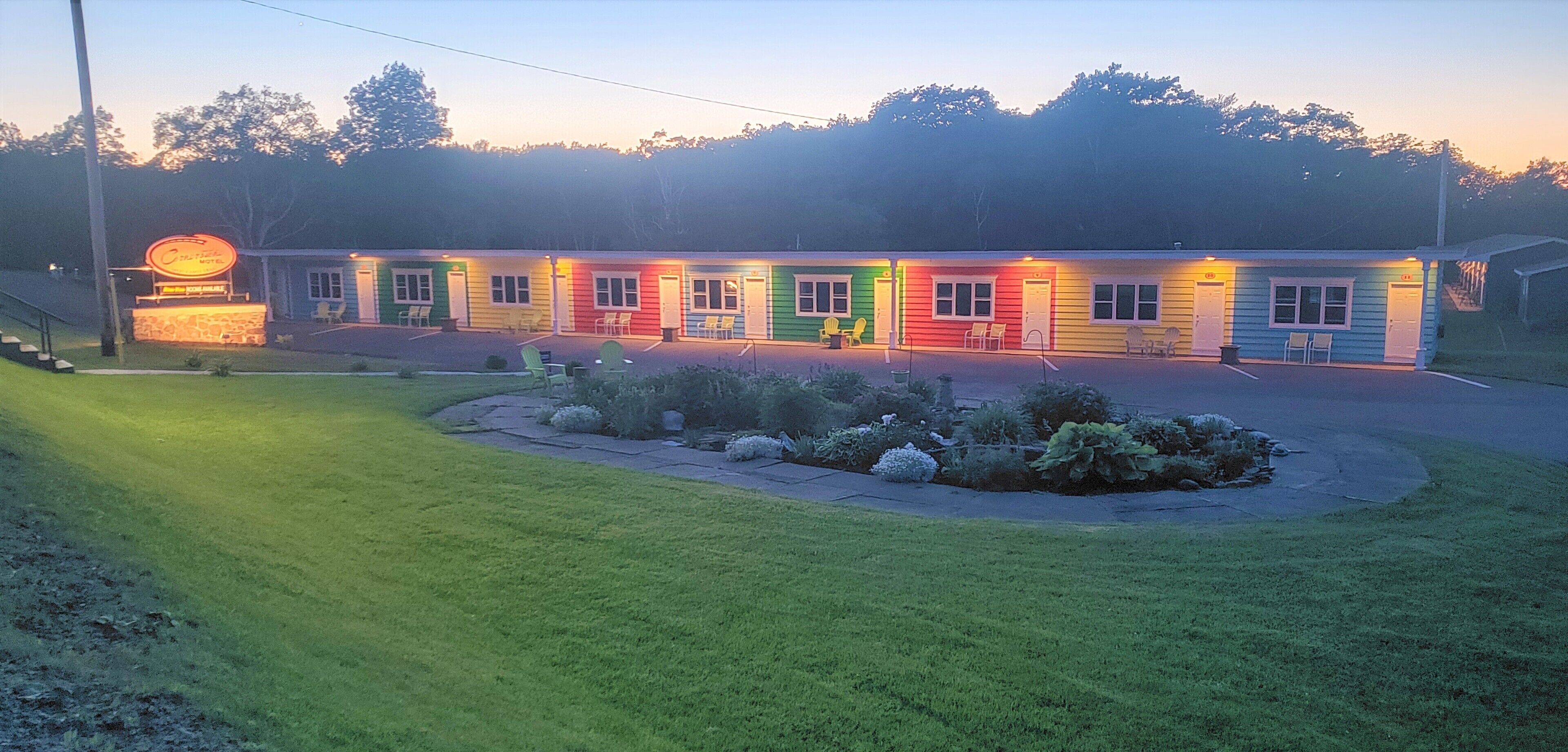 A motel with a row of rooms in various colors, a small parking area, and a well-maintained lawn.