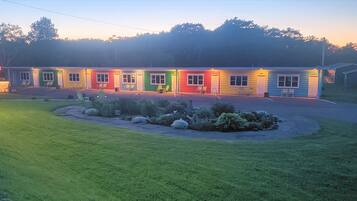 A motel with a row of rooms in various colors, a small parking area, and a well-maintained lawn.
