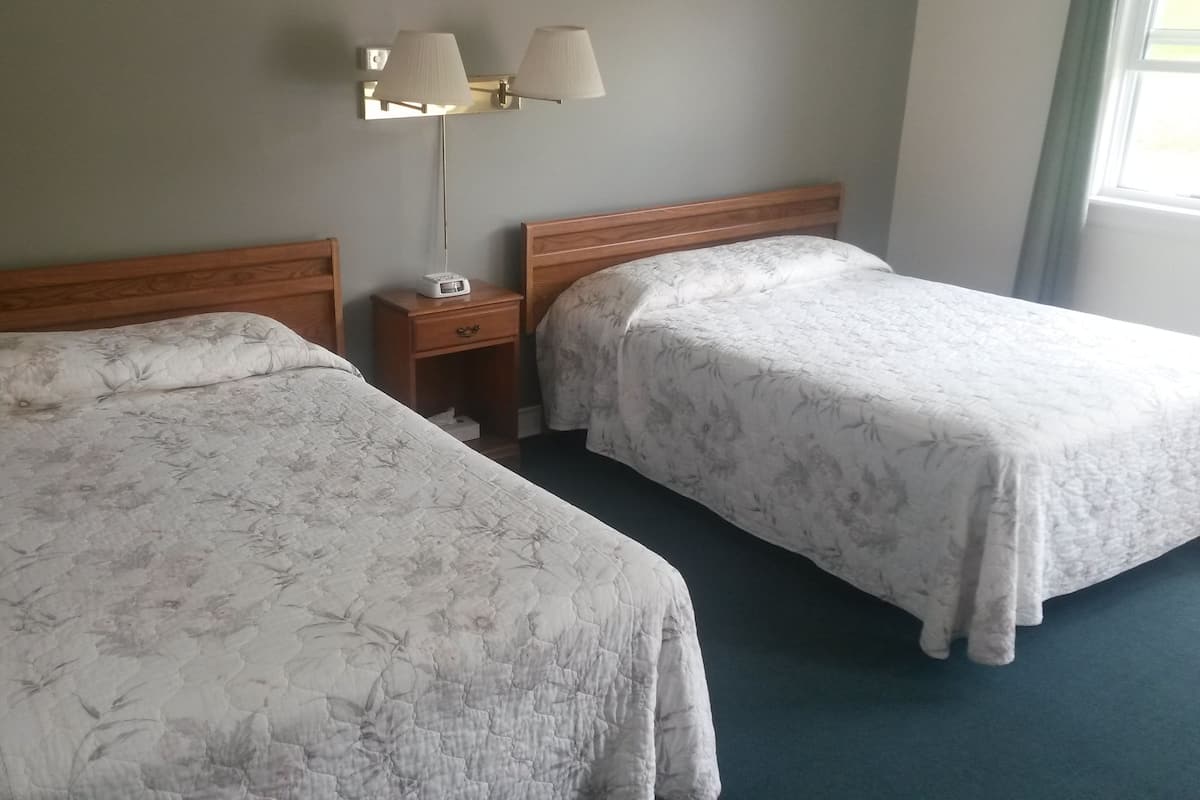 A hotel room with two single beds, a nightstand with a lamp, and a wall-mounted light fixture.
