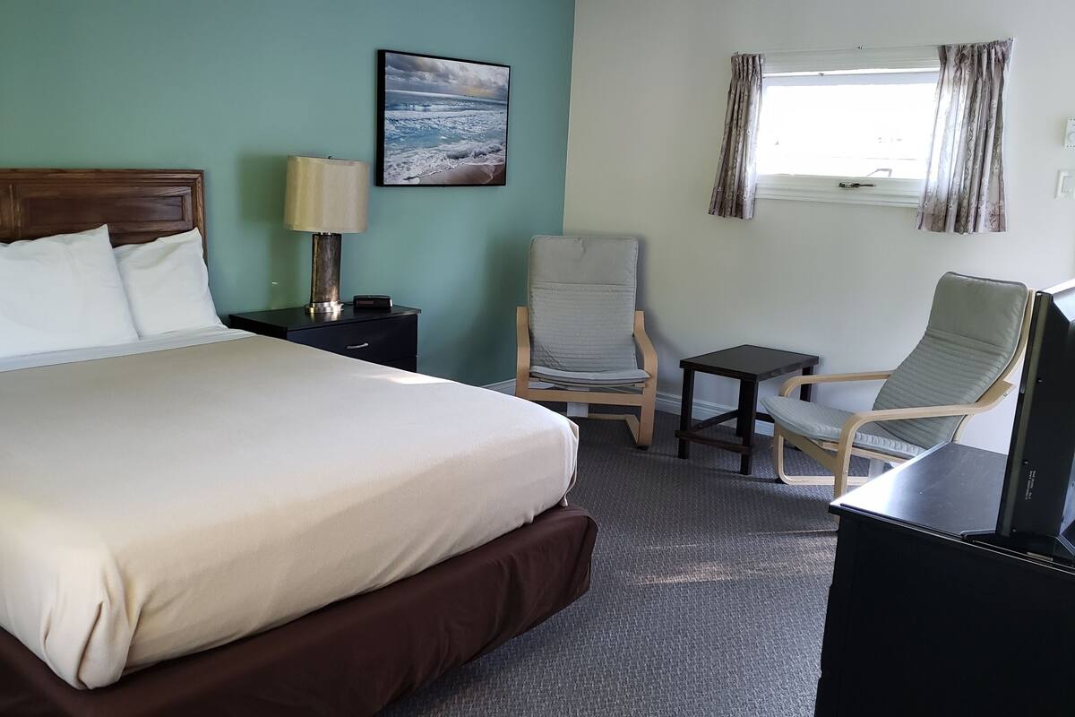A hotel room with a large bed, a desk, a chair, and a TV.
