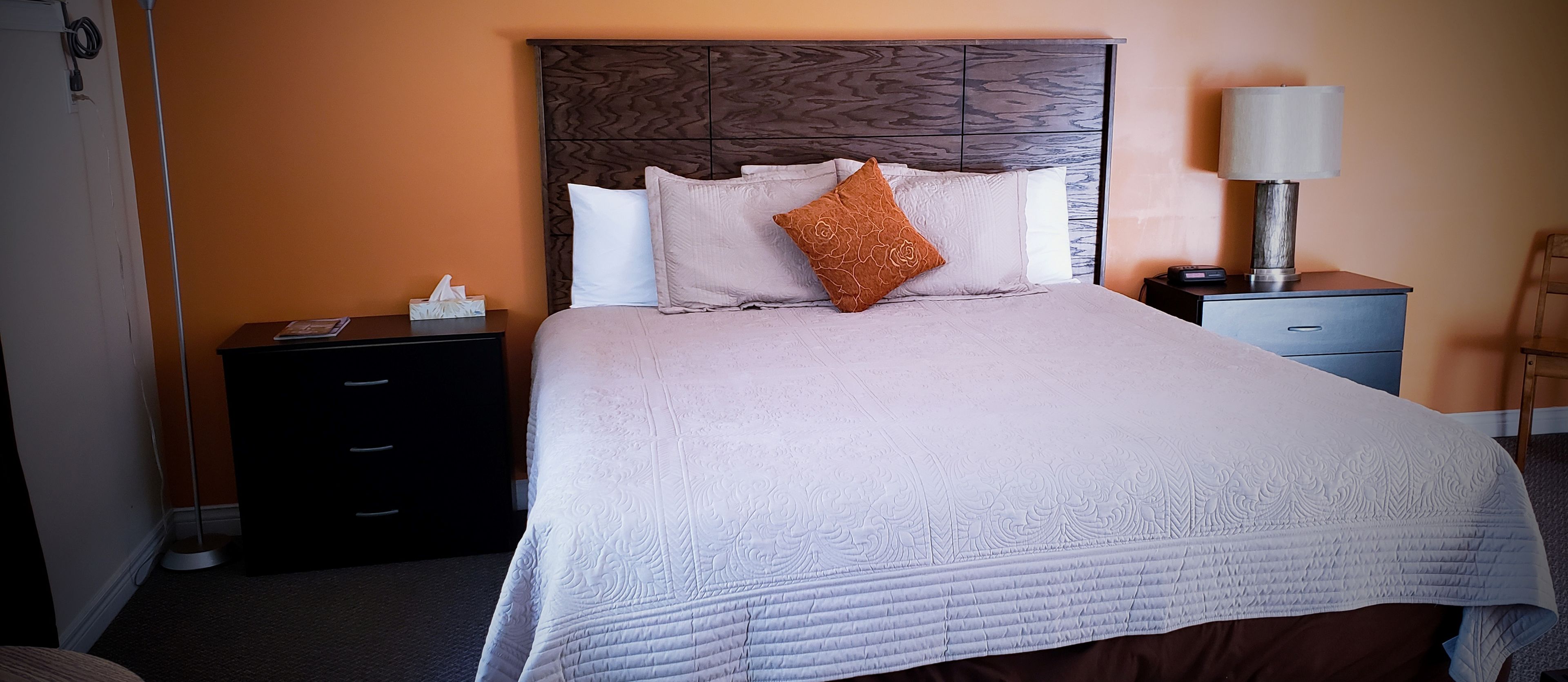 A neatly made bed with a patterned headboard, a bedside lamp, and a nightstand with a tissue box.