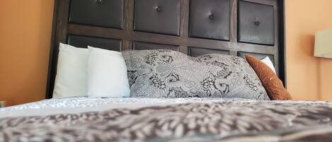 Una cama con una colcha estampada, un cabecero oscuro con paneles cuadrados, y dos almohadas, una con diseño paisley y otra marrón.