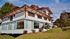 Una casa de dos pisos con fachada blanca, detalles rojos y amplios ventanales de vidrio.