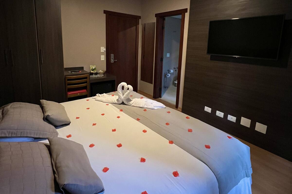 Habitación de hotel con una cama grande, un televisor montado en la pared y un armario de madera.