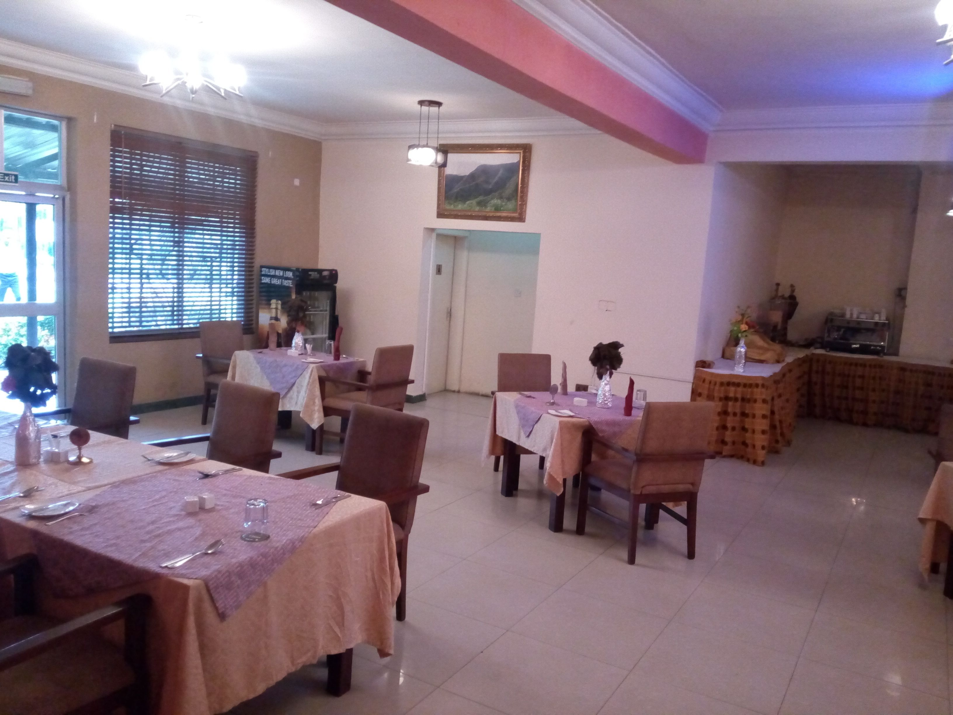 A dining area with tables set for four, chairs, a chandelier, and a view of the outdoors through a window.