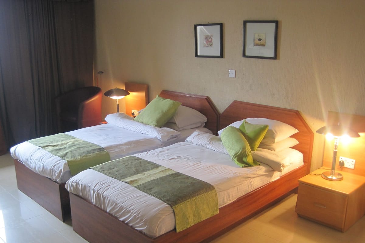 A double bed with a wooden frame, two bedside tables with lamps, and two framed pictures on the wall.
