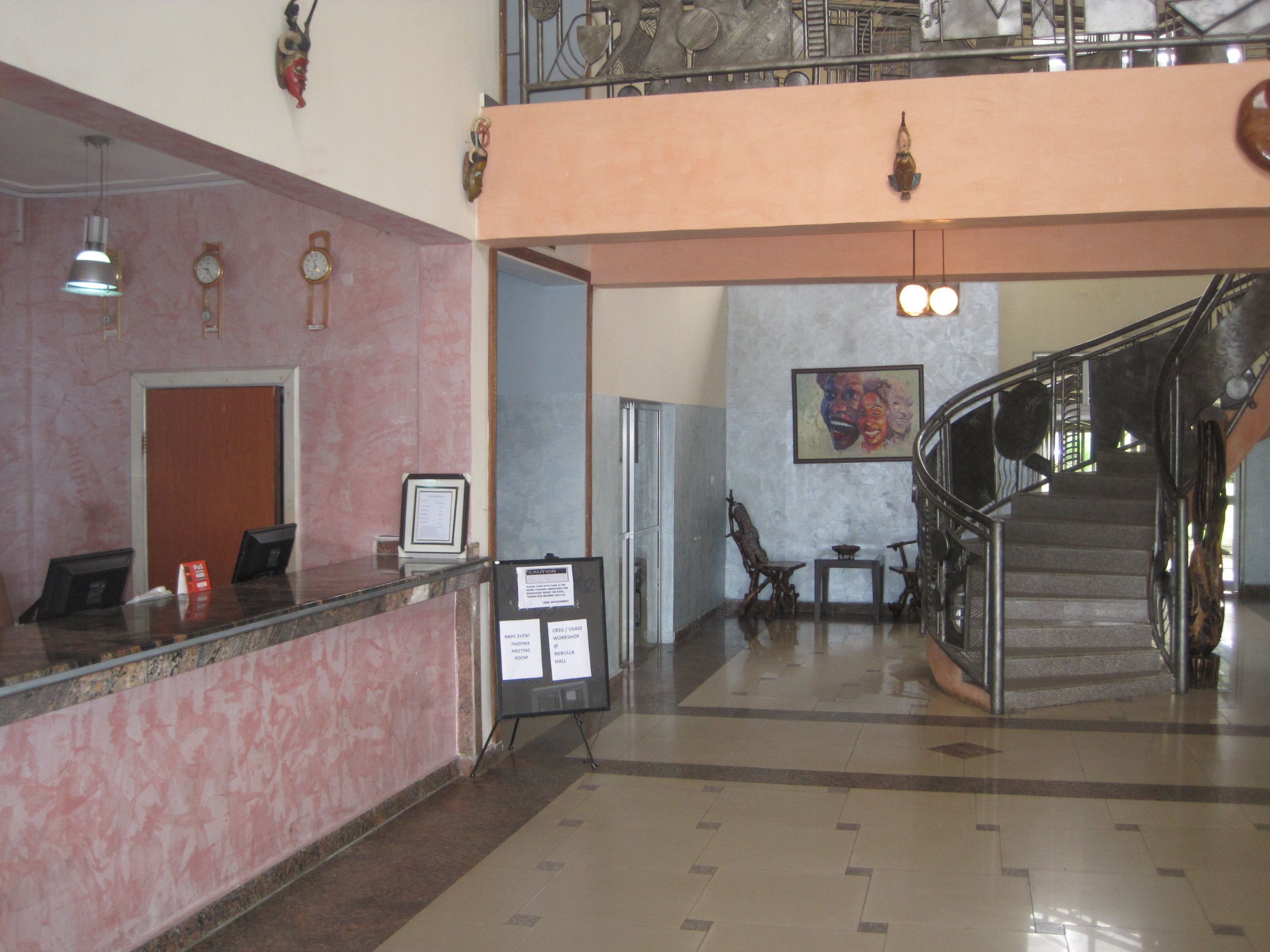 A lobby with a reception desk, a staircase, and a wall with clocks and a framed picture.
