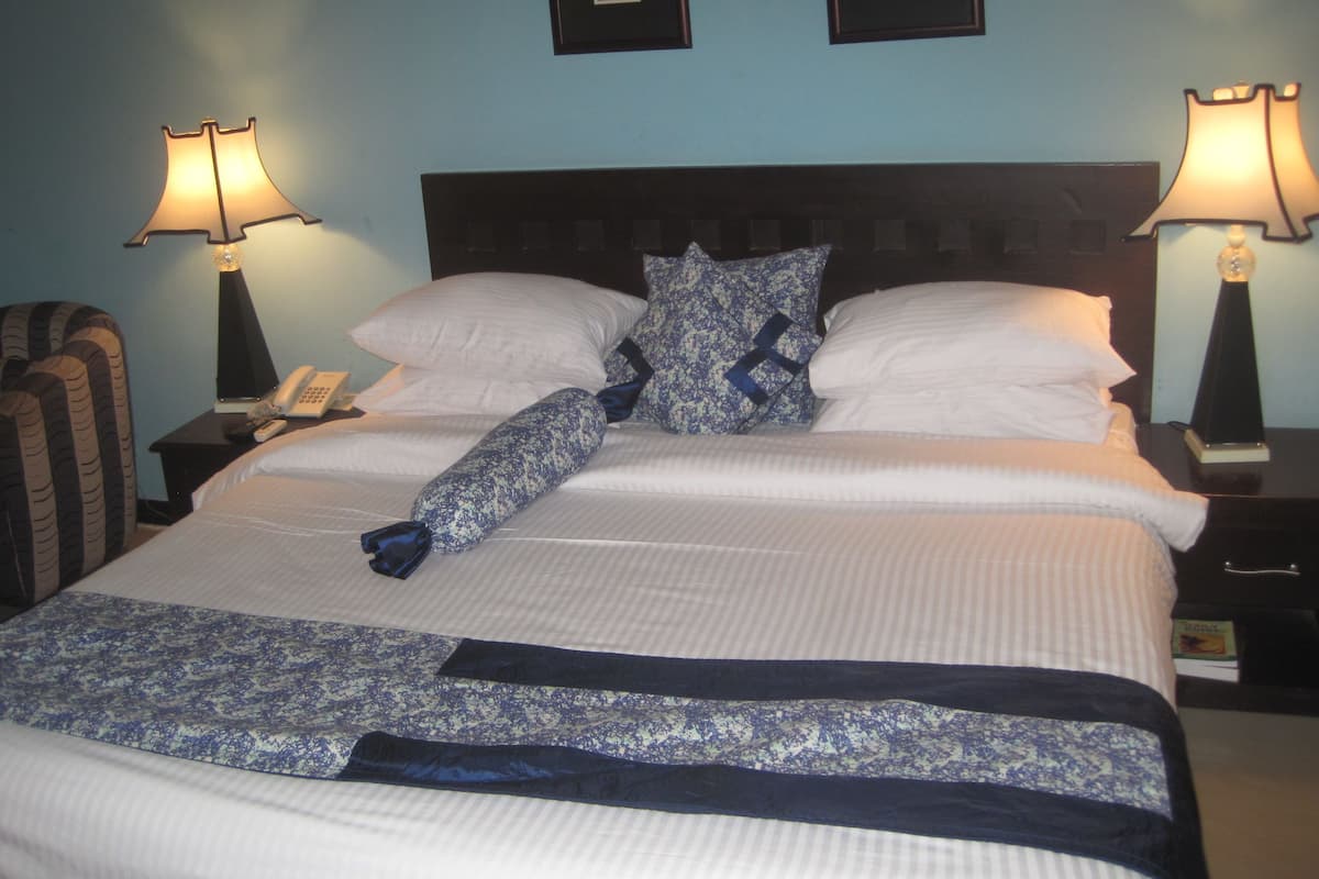 A neatly made bed with a patterned blanket, two pillows, and a headboard. There are two bedside tables with lamps and a telephone on one of them. The walls are painted blue, and there are two framed pictures on the wall.