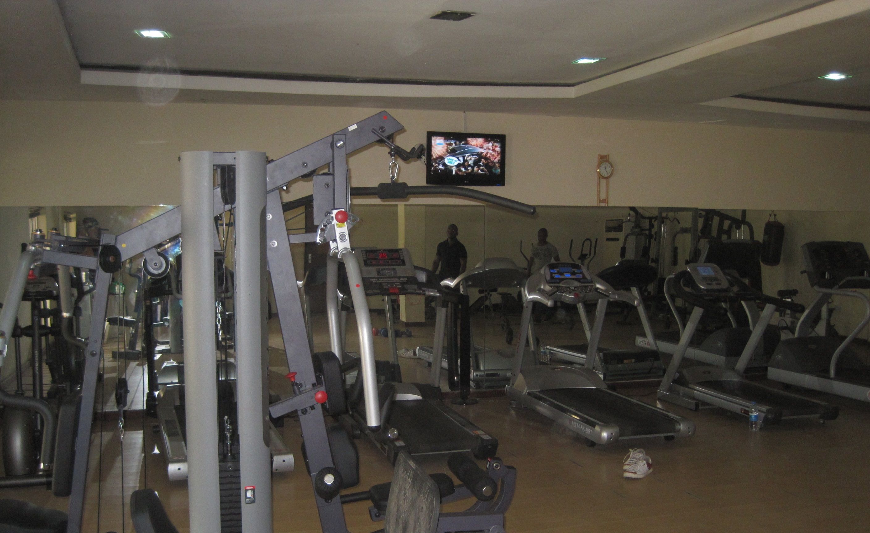 A gym with various exercise equipment including treadmills, a weight machine, and a television screen displaying a sports event.