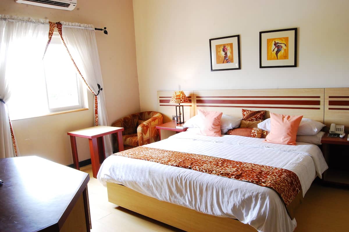 A hotel room with a bed, a desk, a chair, a nightstand, and two framed pictures on the wall.