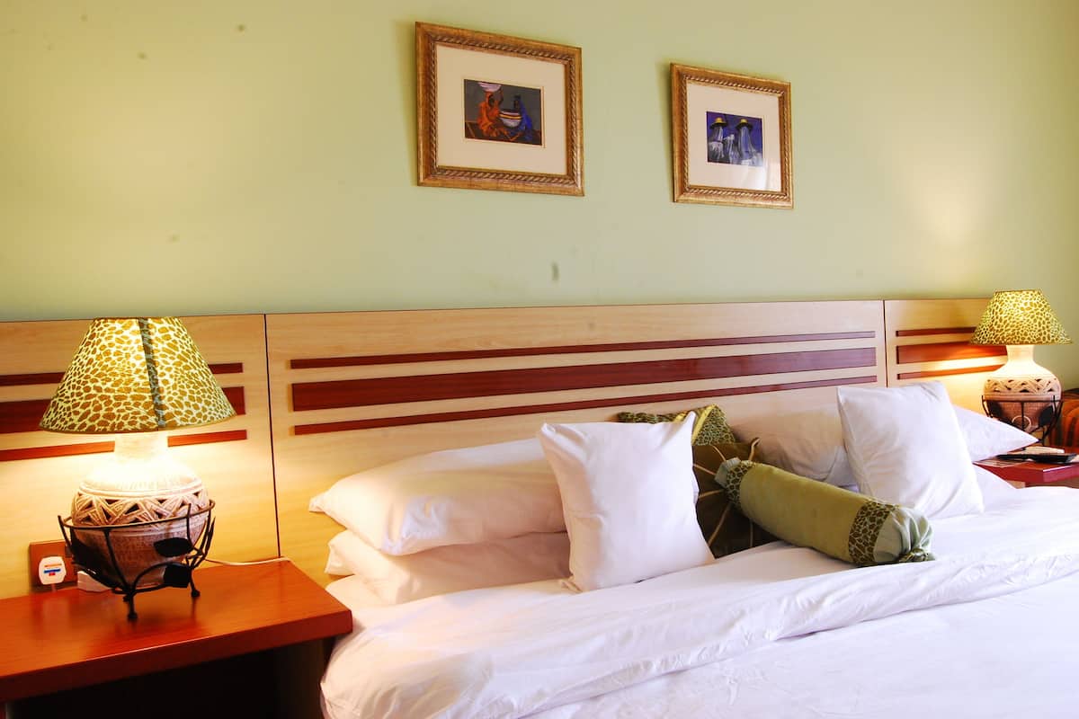A hotel room with a bed, two framed pictures on the wall, and two lamps on nightstands.