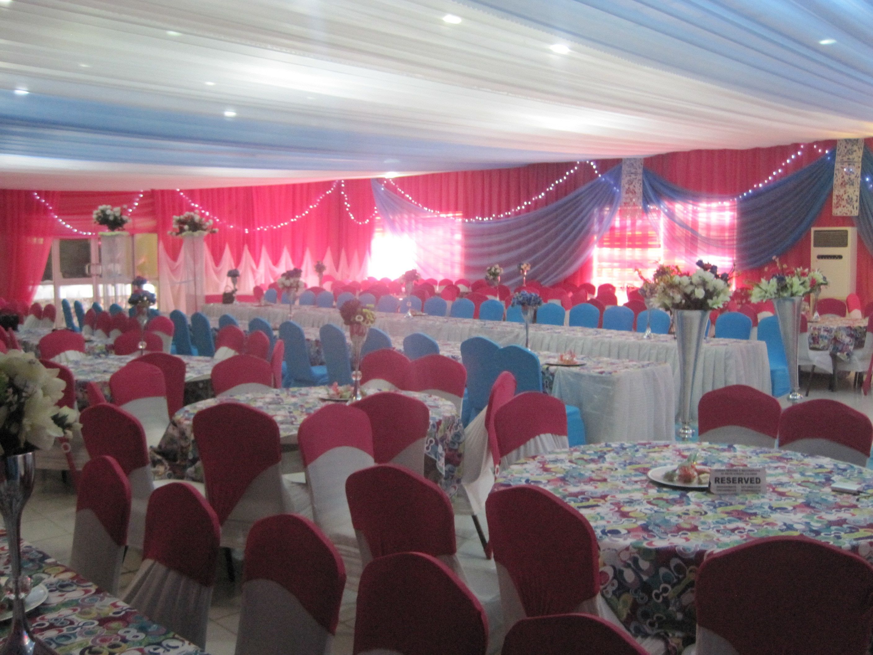 A banquet hall with round tables, red and blue chairs, and floral centerpieces.