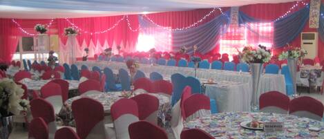 A banquet hall with round tables, red and blue chairs, and floral centerpieces.