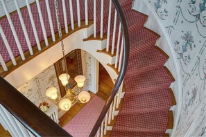 A spiral staircase with a wooden finish and white railings, leading to a landing area with a chandelier and patterned wallpaper. - Sherburne Inn (Nantucket)