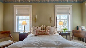 A bedroom with a large bed, two bedside tables, a nightstand, a chair, and two windows with shutters. - Sherburne Inn (Nantucket)