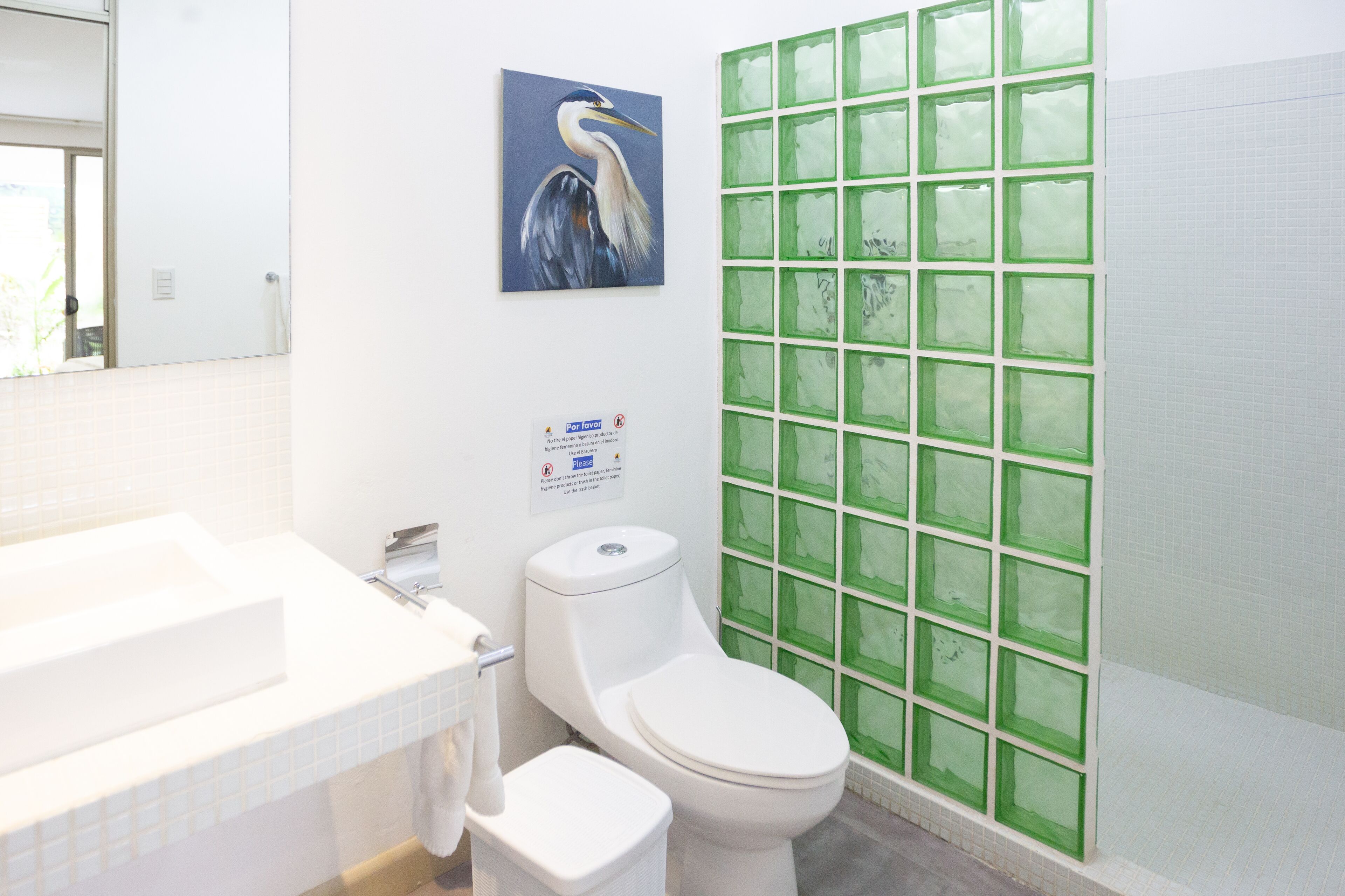 Un baño con un lavabo blanco, inodoro y pared de bloques de vidrio verde.