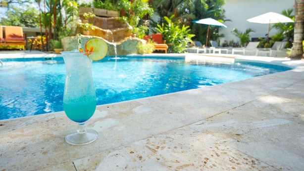 Vista despejada de una piscina con una bebida en un vaso, rodeada de sillones de descanso y sombrillas.