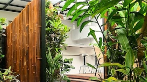 Un espacio exterior moderno con cerramiento de vidrio, valla de bambú y abundante vegetación.