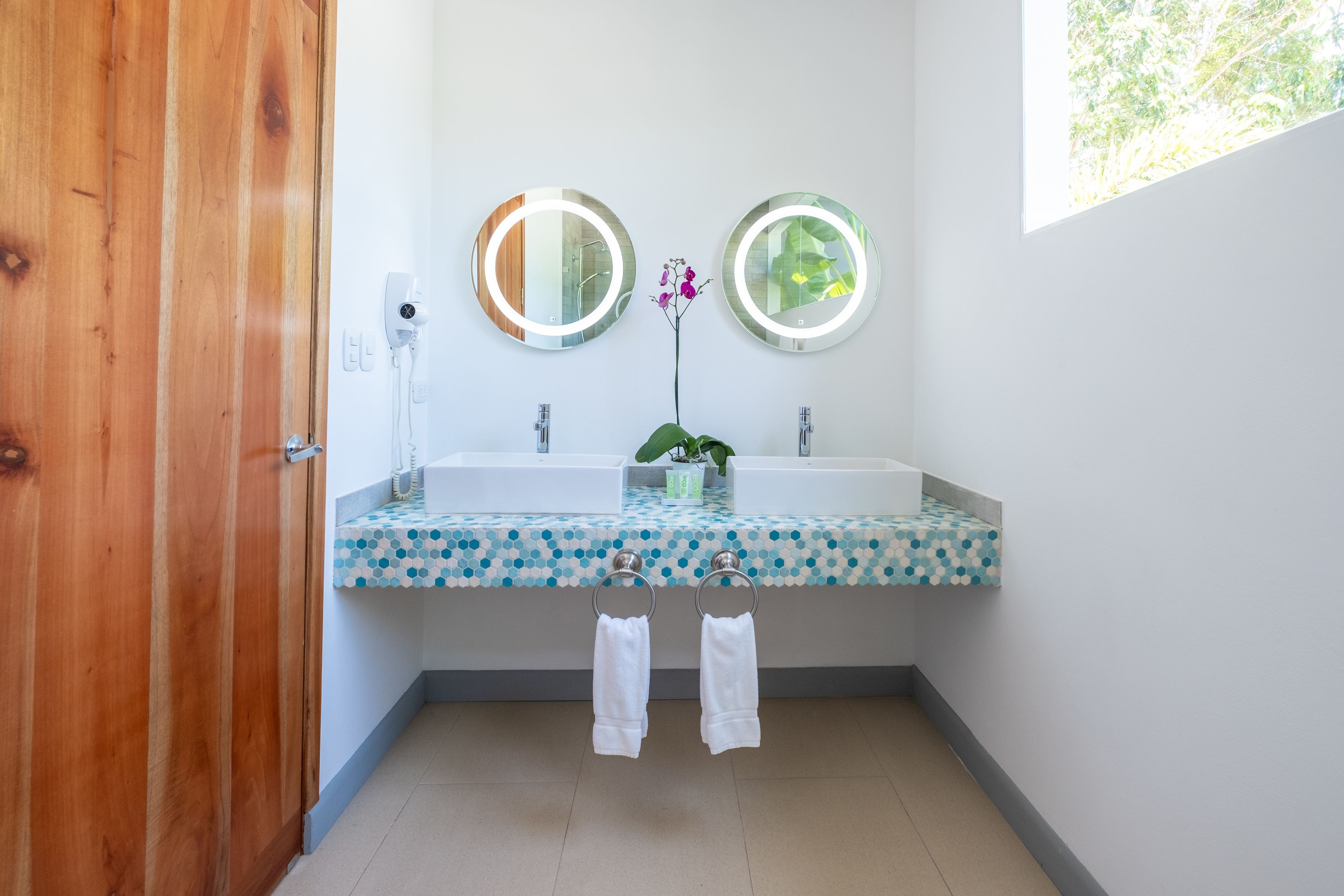 Un baño con dos lavamanos, una puerta de madera y un espejo con luz.