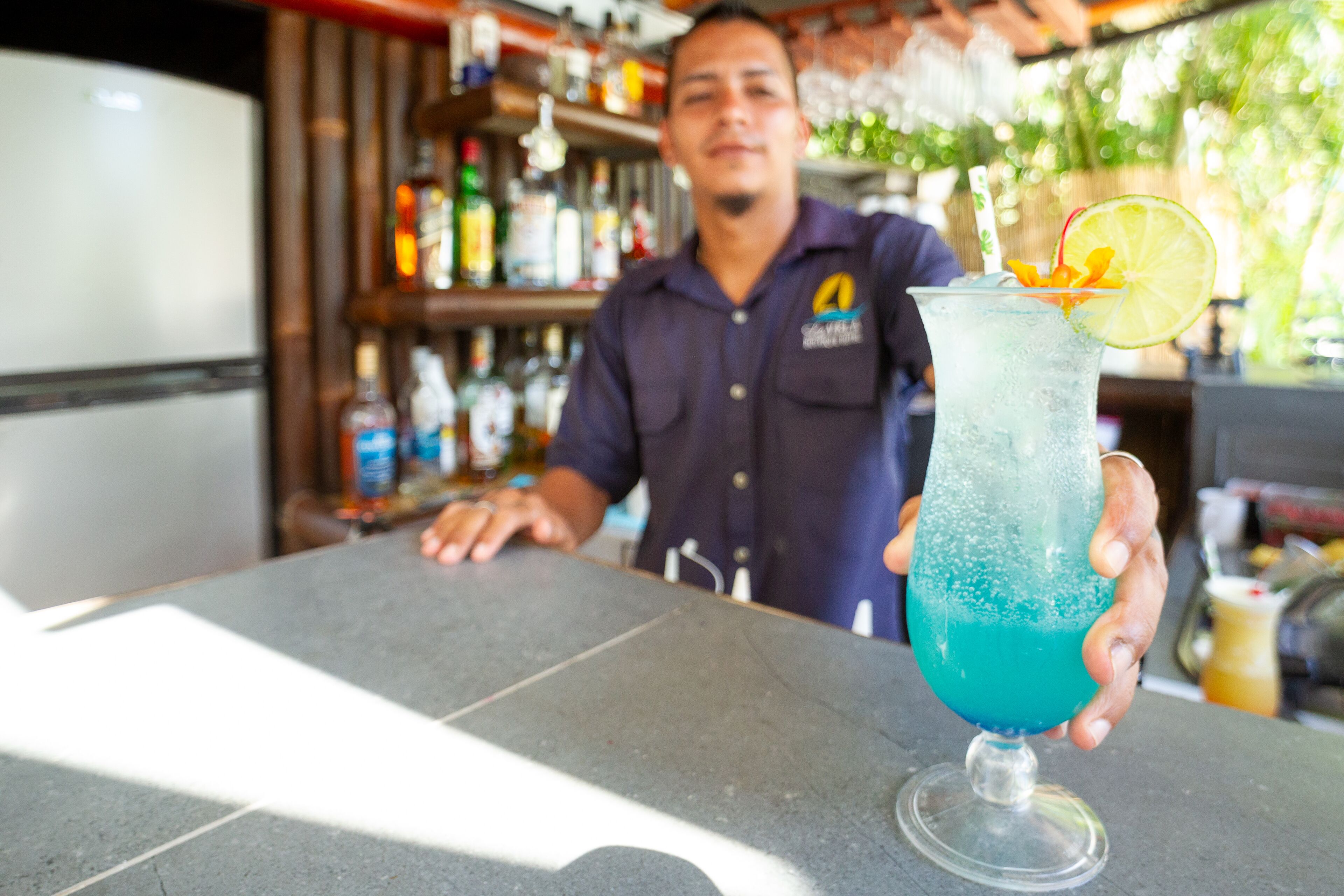 A bartender holding a blue cocktail with a lime slice garnish.