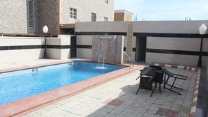 A swimming pool with a water feature, surrounded by a tiled patio area with outdoor seating. - Eastgate Hotel Lekki (Lekki)