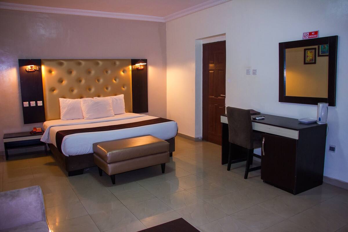 A hotel room with a large bed, a desk, a chair, and a small table.