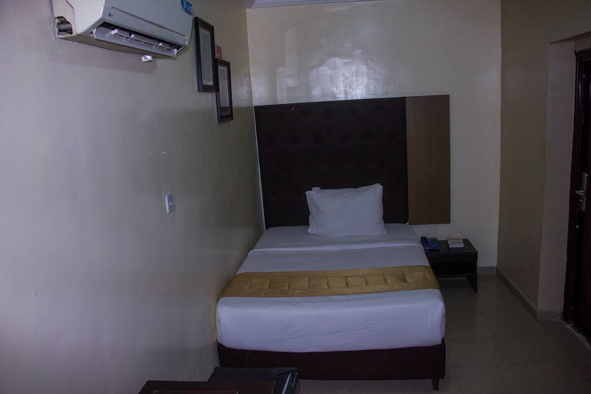 A hotel room with a bed, a nightstand, a wall-mounted air conditioner, and a door.
