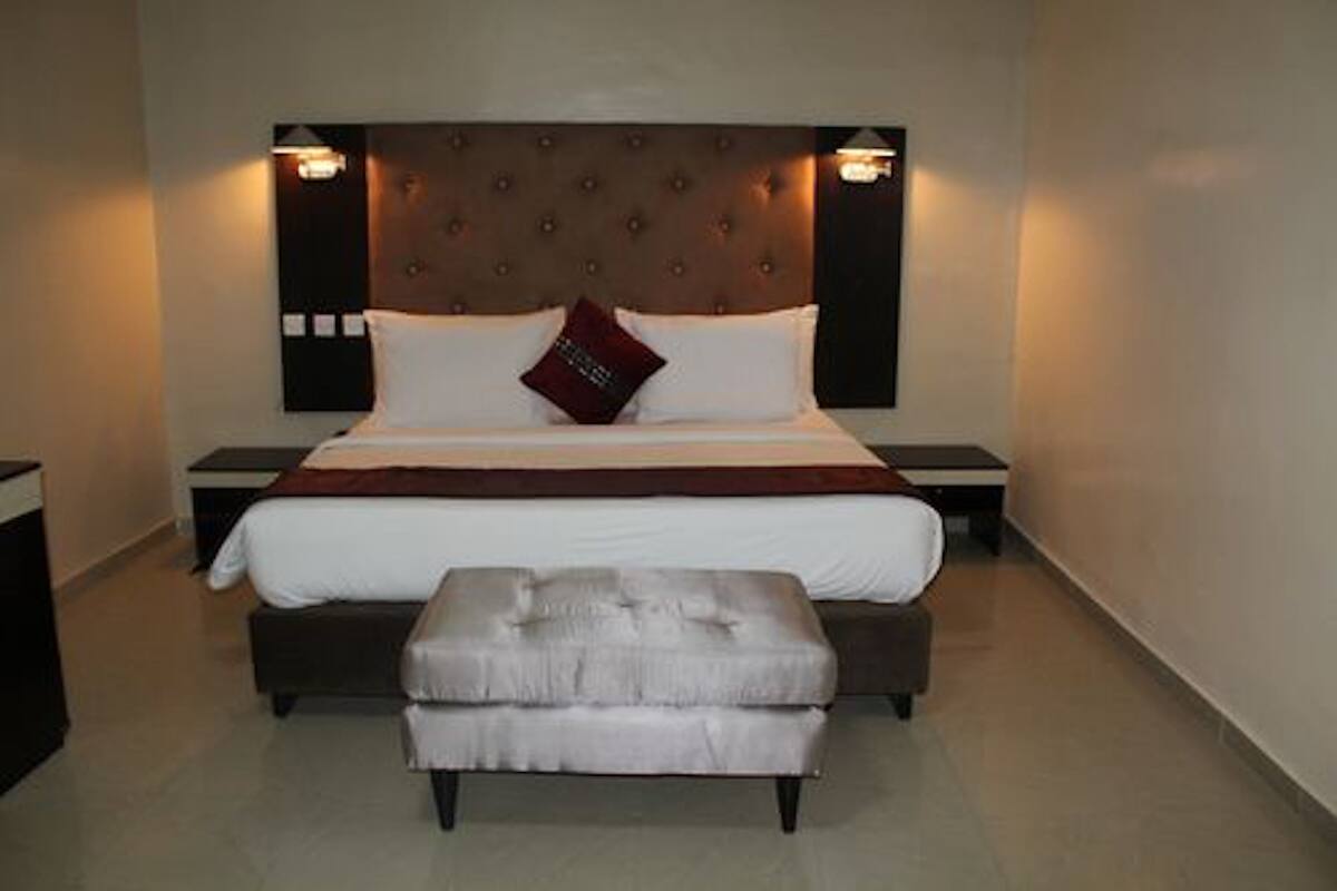 A hotel room with a large bed, a bedside table, a nightstand, and a footstool.