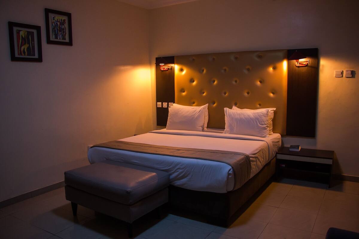 A bedroom with a large bed, a bench, and a nightstand.