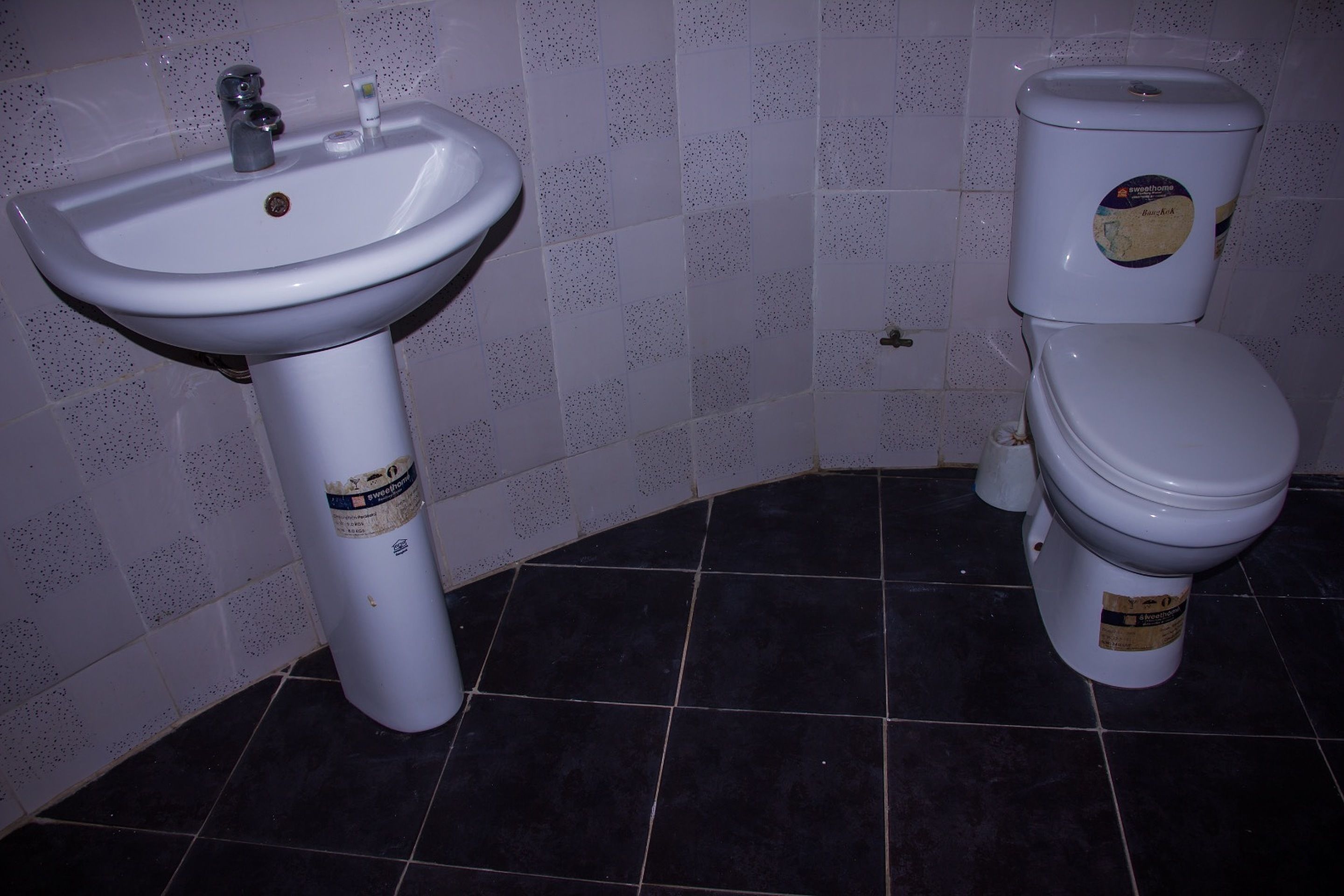 A bathroom with a white sink, a toilet, and dark tiled flooring.