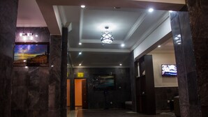 A lobby with marble columns, a ceiling light fixture, and a flat-screen TV mounted on the wall. - Eastgate Hotel Lekki (Lekki)