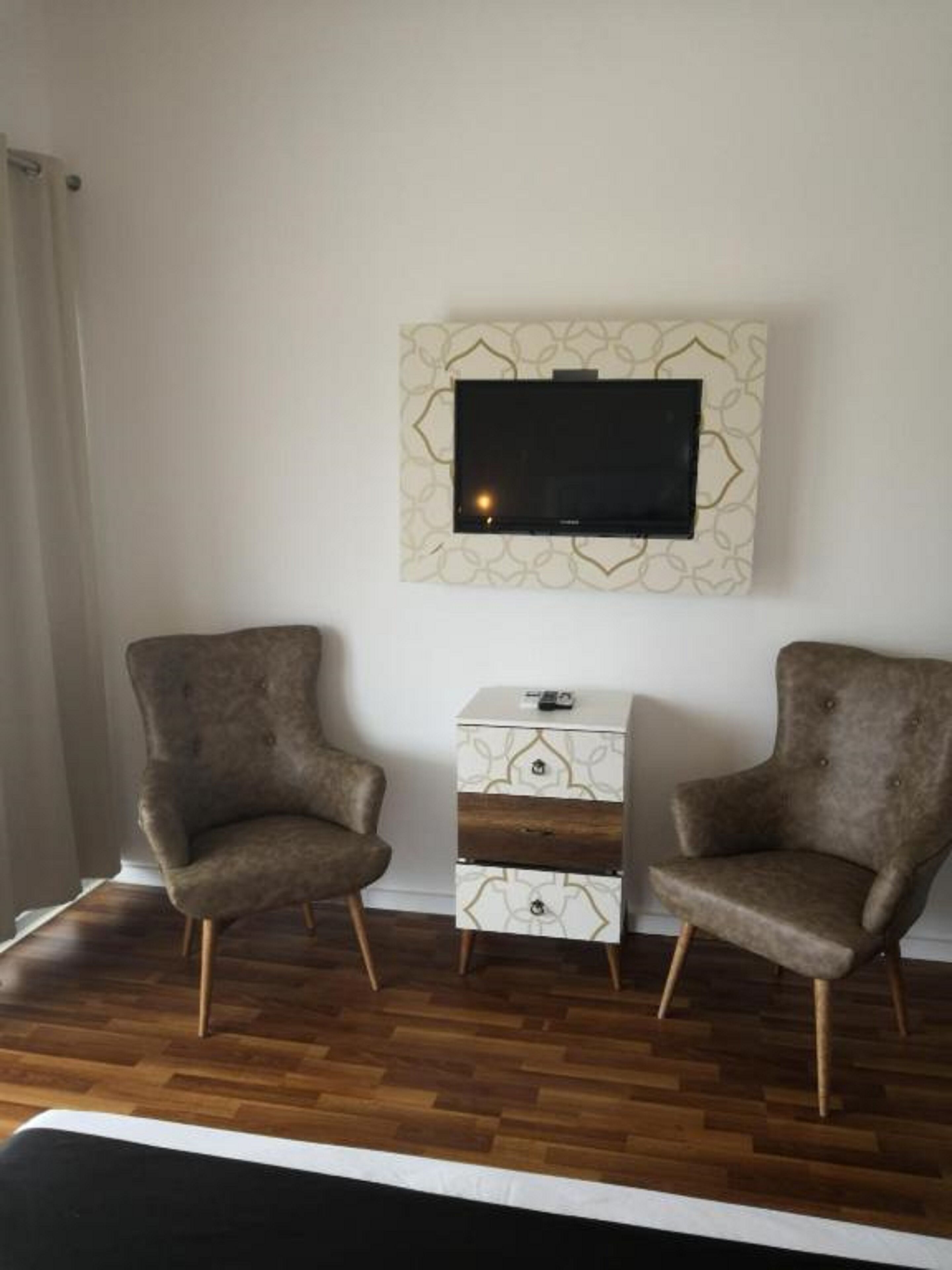 A room with two armchairs, a small white side table, and a flat-screen TV mounted on the wall.