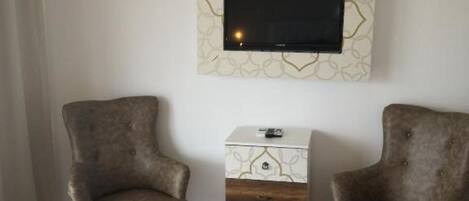 A room with two armchairs, a small white side table, and a flat-screen TV mounted on the wall.