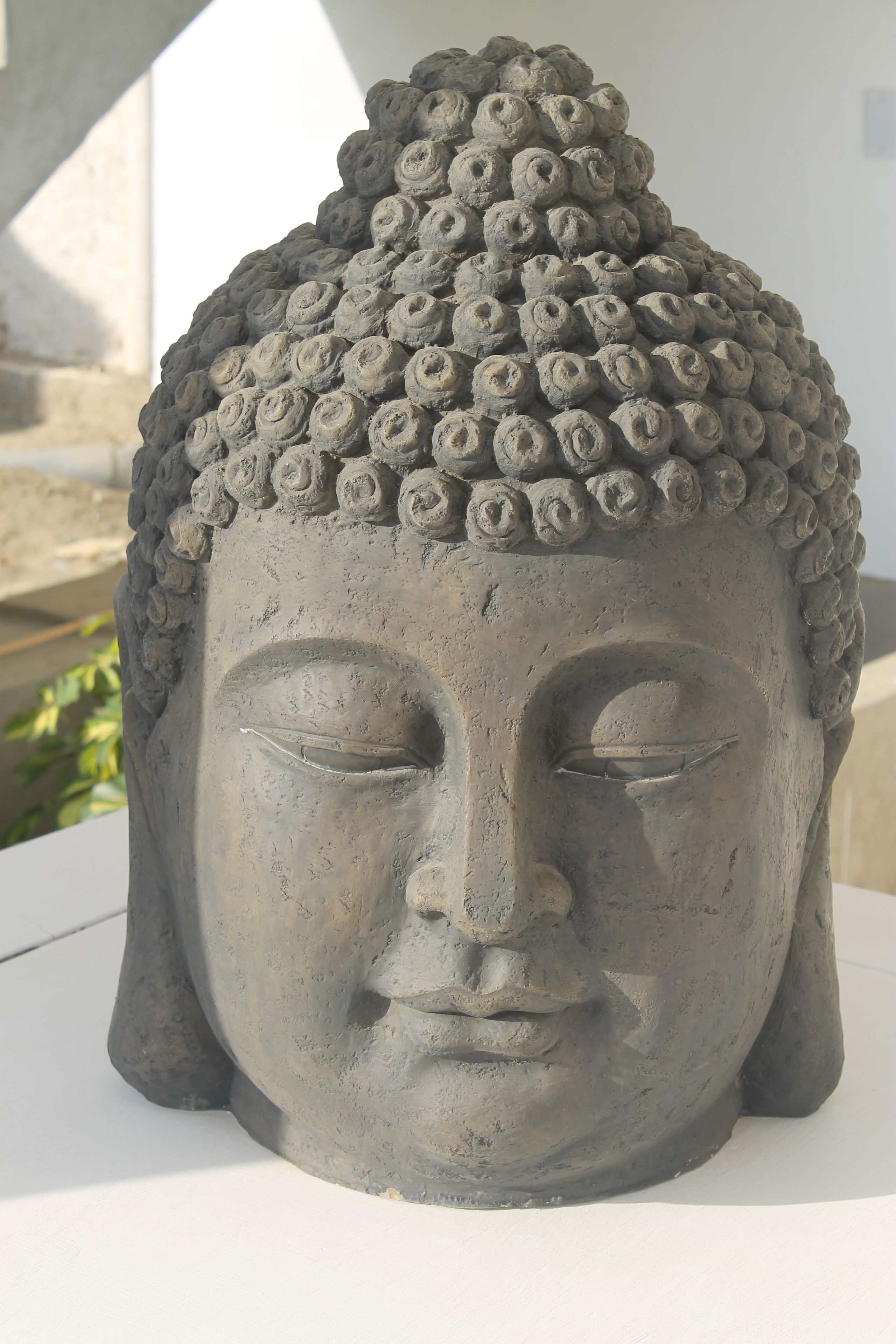 Escultura de cabeza de Buda de piedra con superficie texturizada y parte superior redondeada.