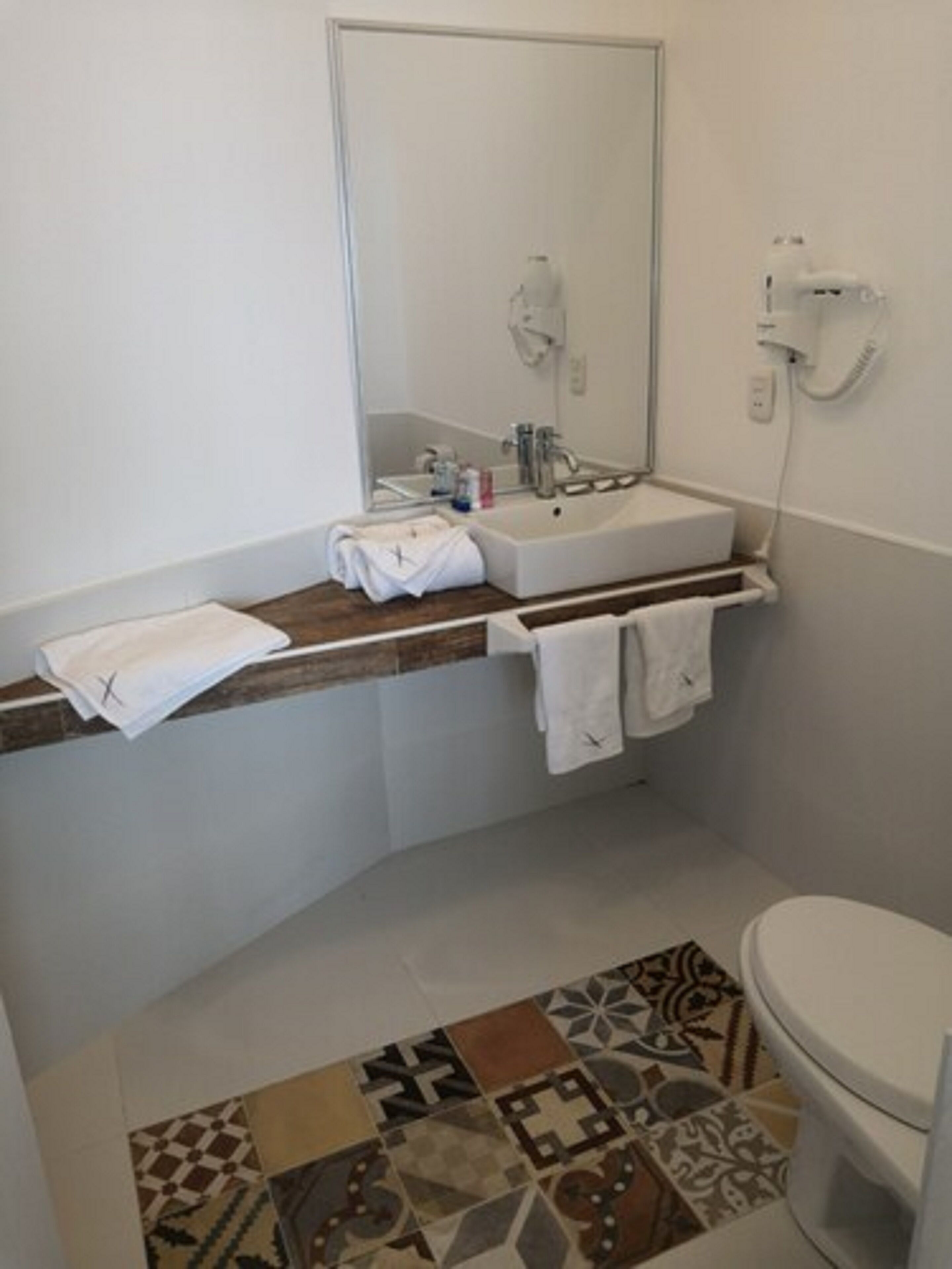 A bathroom with a white sink, mirror, and toilet. There are towels on the counter and a patterned rug on the floor.