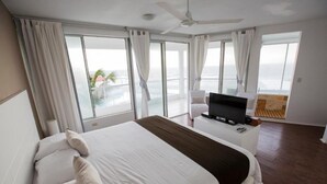 Habitación de hotel con una cama grande, un televisor en una mesita auxiliar y un balcón con vista al océano.